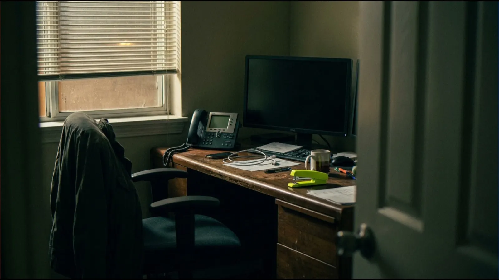 An empty office desk after hours with a desk phone and a switched-off monitor