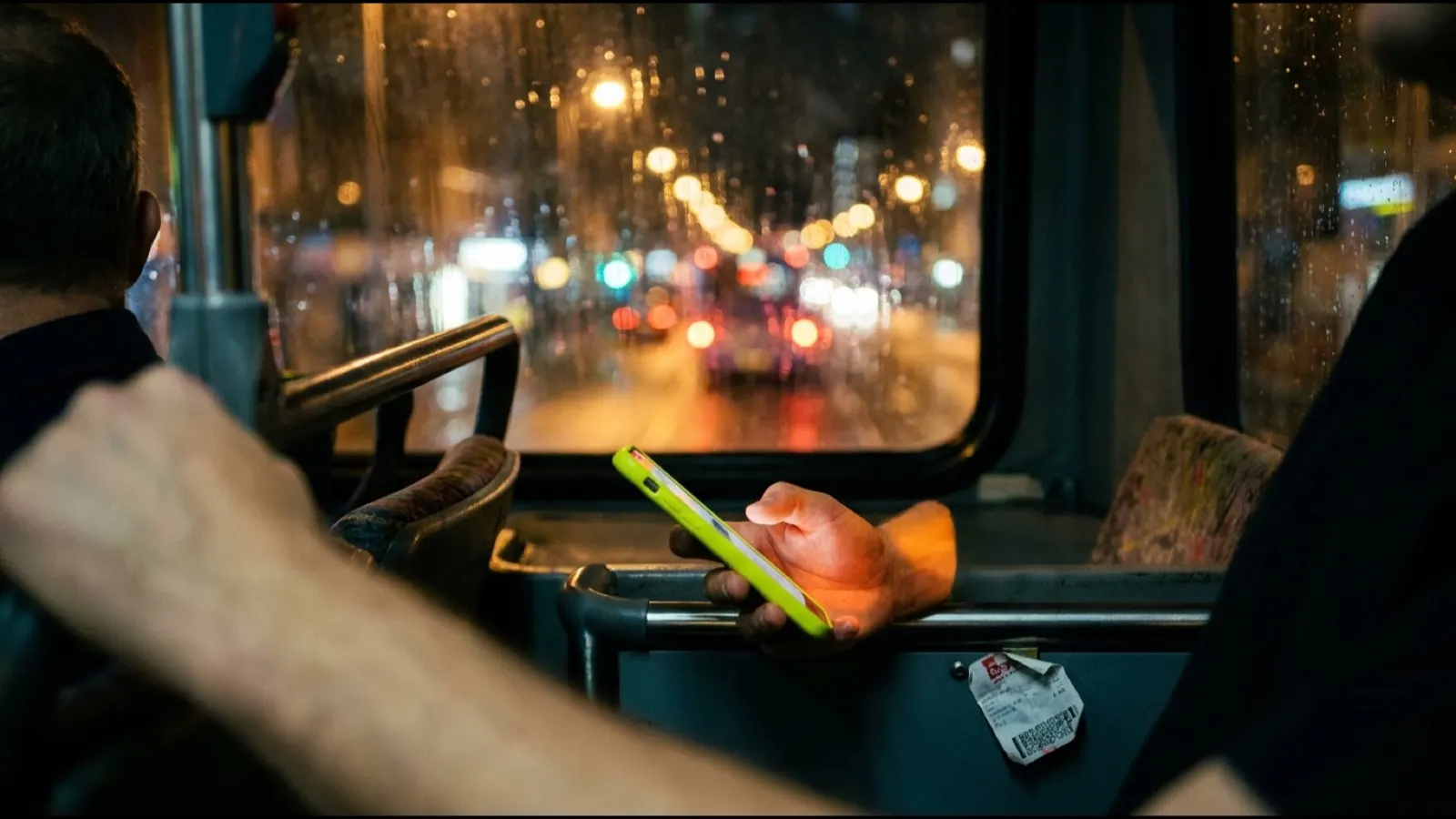 A phone held in one hand on a bus at night, its screen lighting the fingers