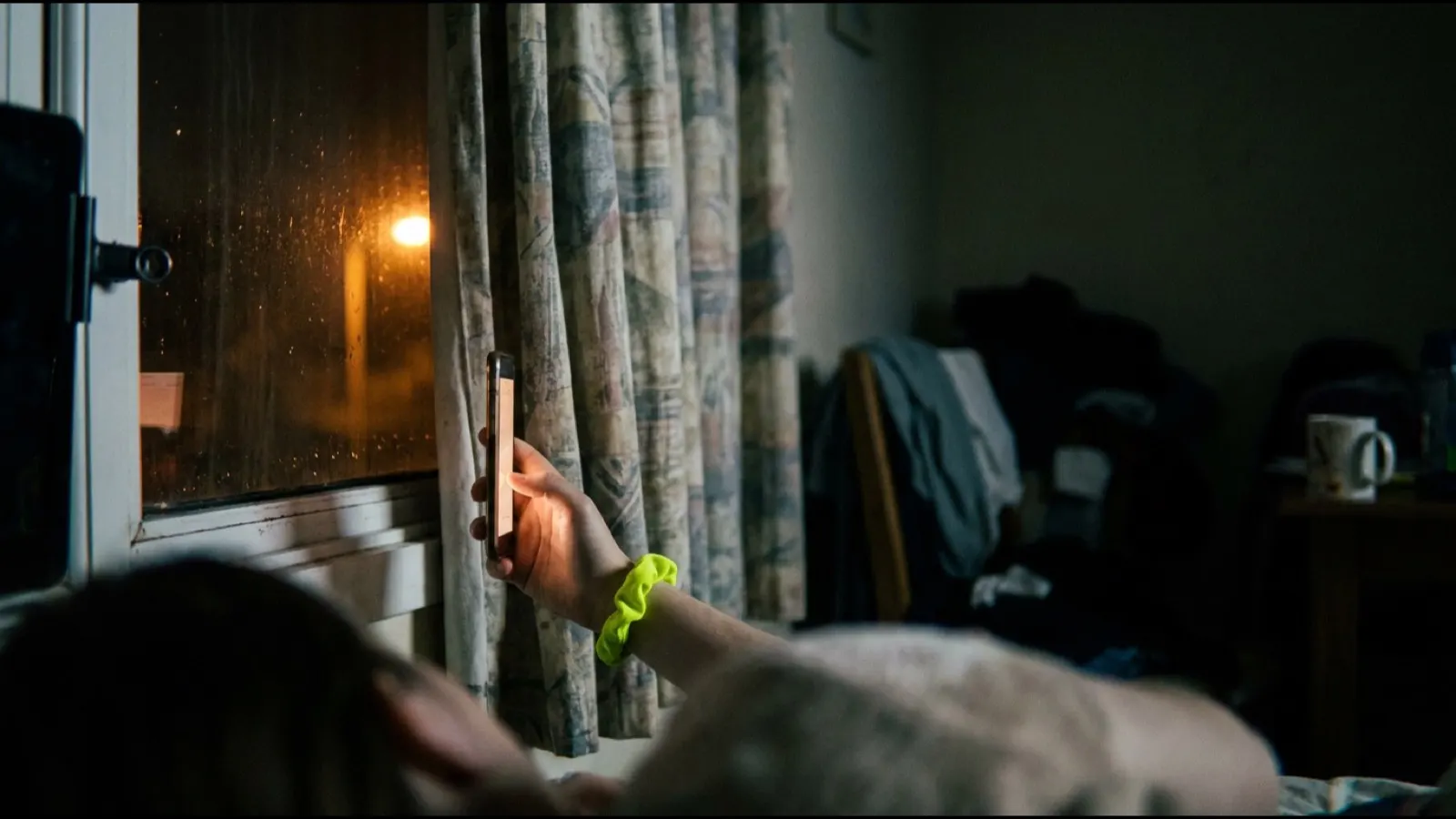A hand holding a phone up to a window at night
